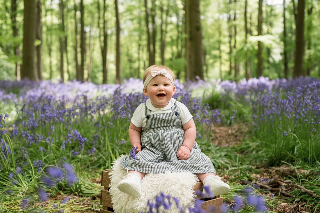1 year old girl sitting in a bluebell wood laughing
