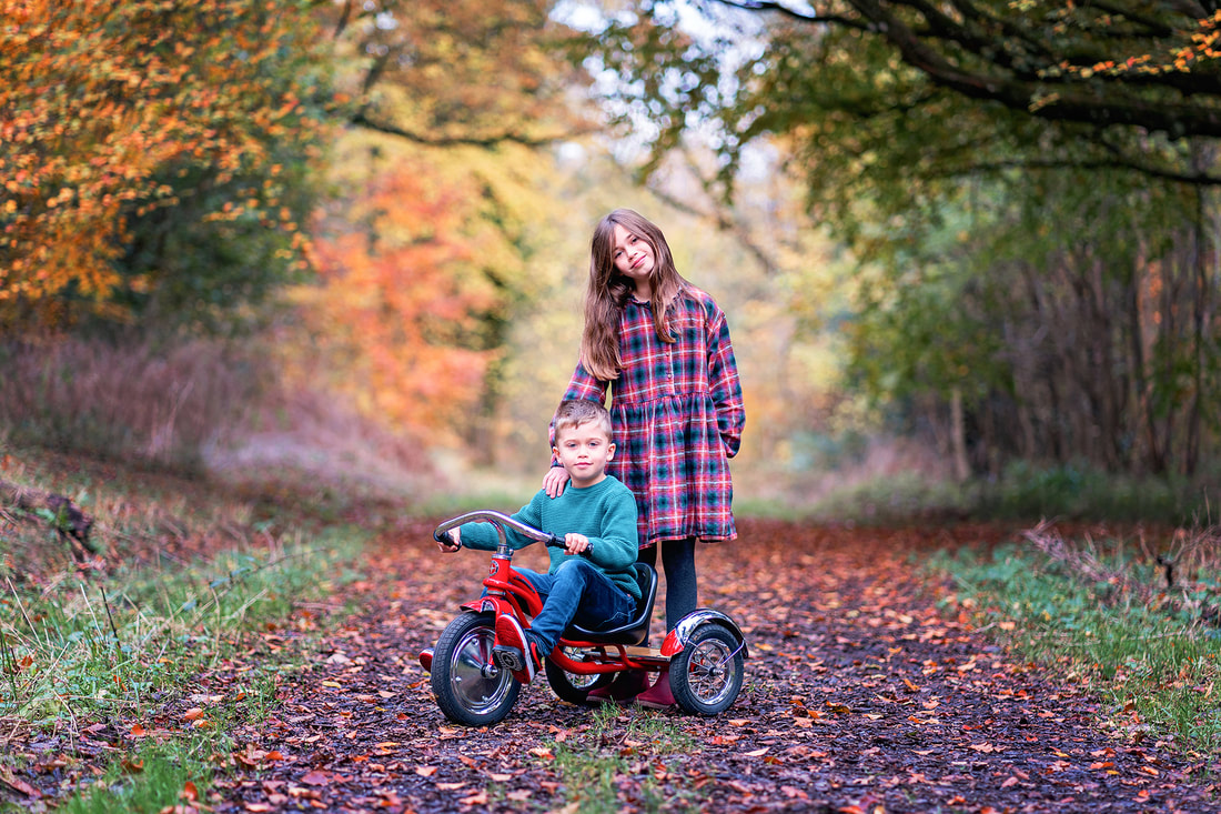 Boy on trike with his sister standing in a forest at Autumn time