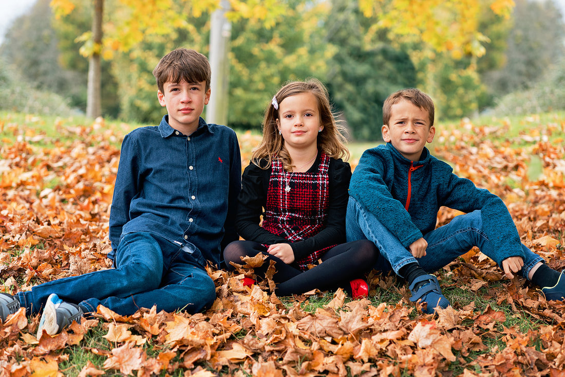 three siblings sitting on brown leaves in the autumn time