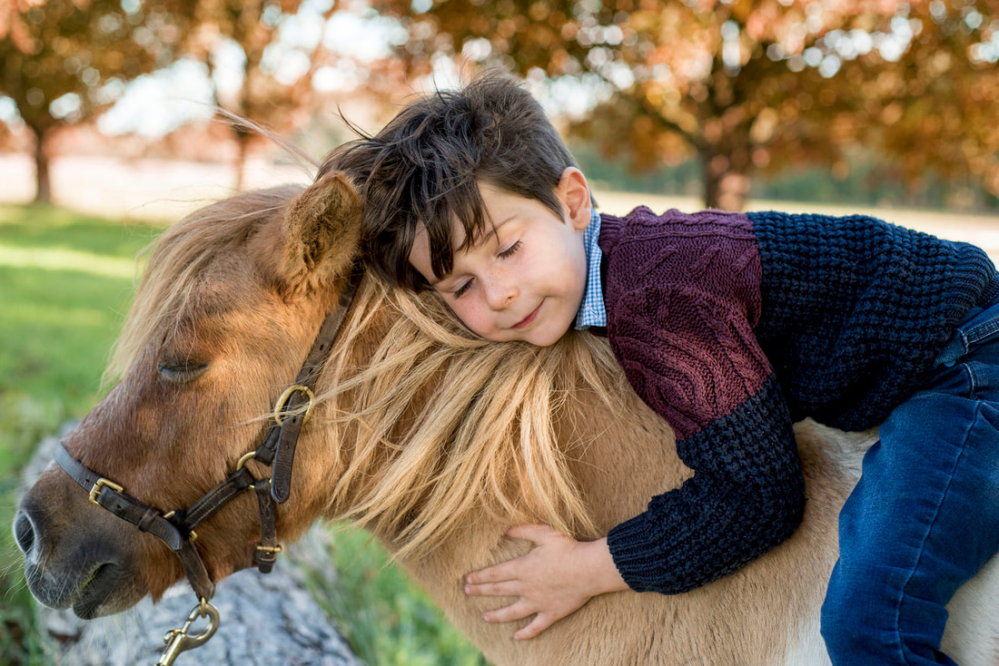 boy sitting on a horse leaning down hugging the horse with their eyes closed