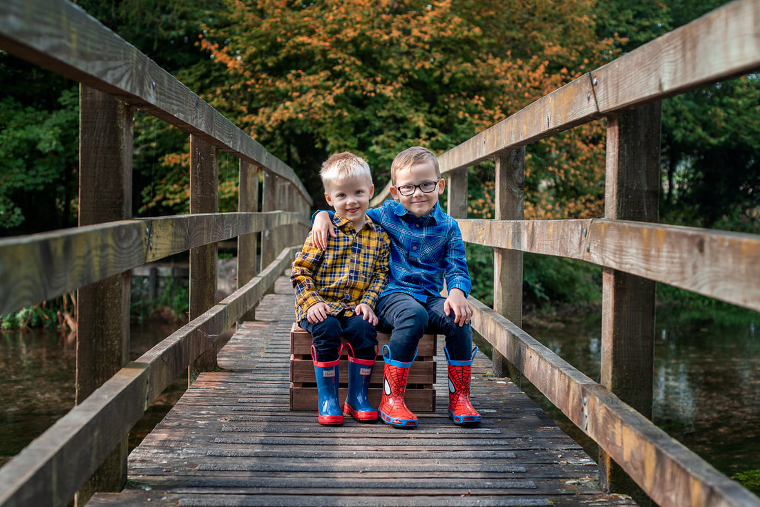 two boys wearing wellies sat on a bridge 