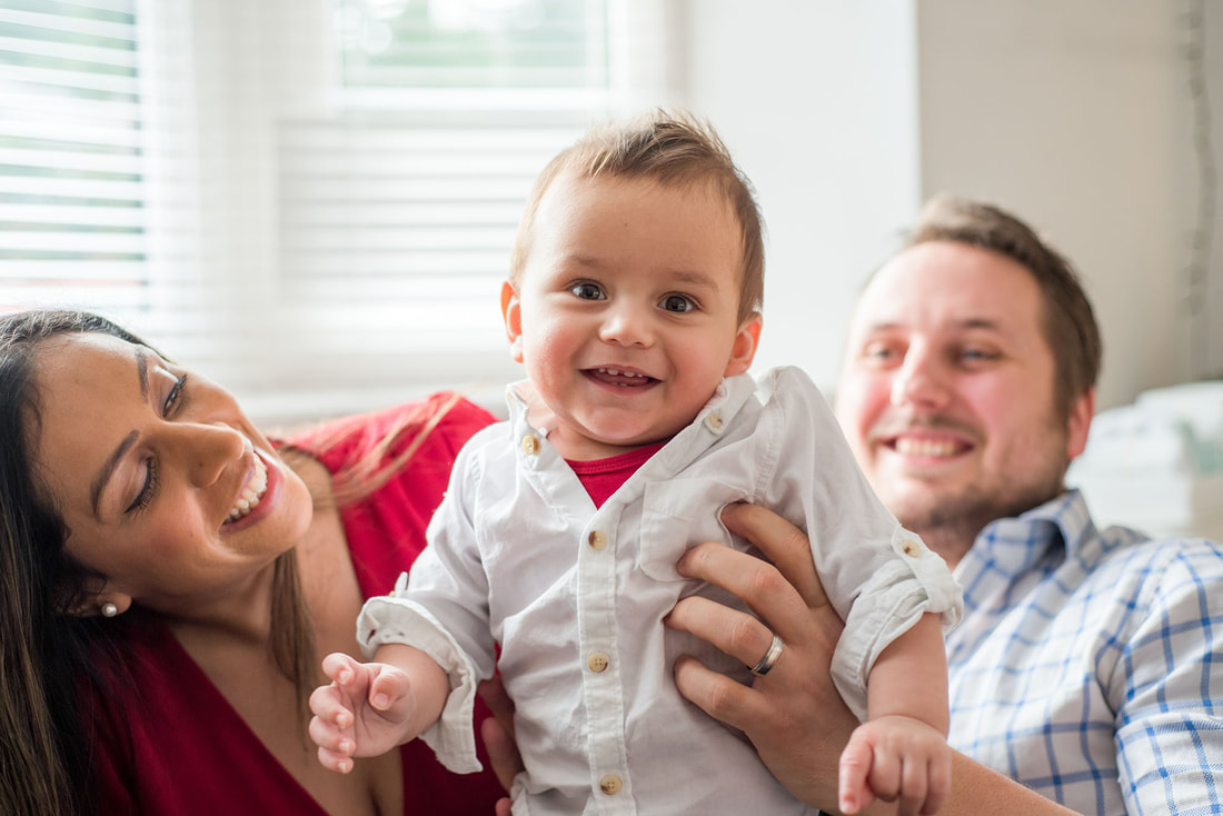 young toddler smiling being held up to camera by mum and dad 