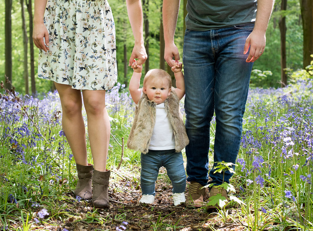 toddler taking firdt steps holding mum and dad's hands in bluebell woods