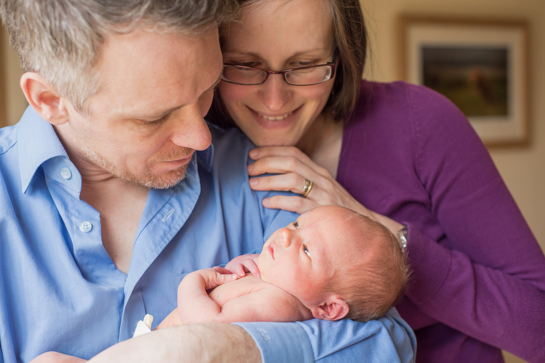 dad holding newborn son in his arm with mum looking over dad's shoulder at baby