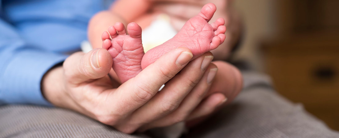 father hands cupping newborn babies feet