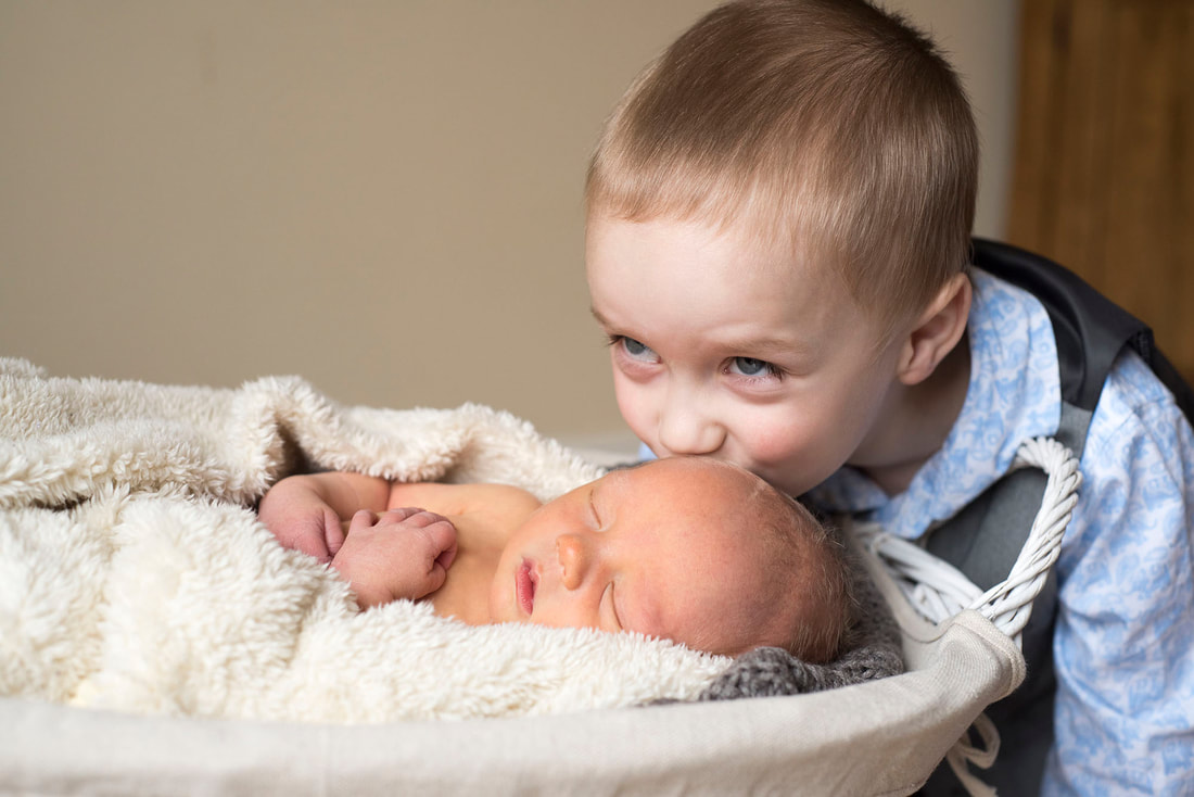 young boy kissing his newborn baby brothers forehead