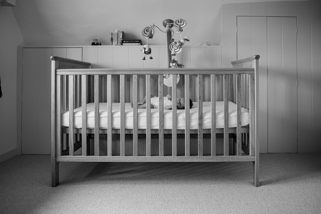 small baby laying in a cot with mobile above head