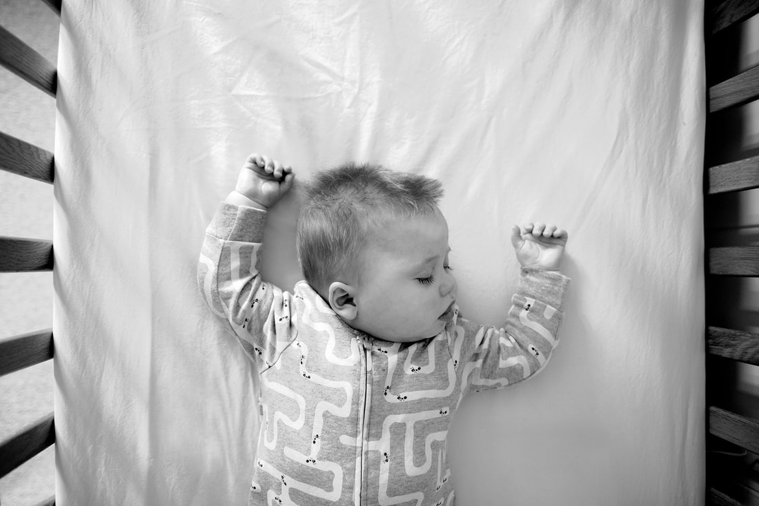 young child sleeping in cot with arms above head and mouth open
